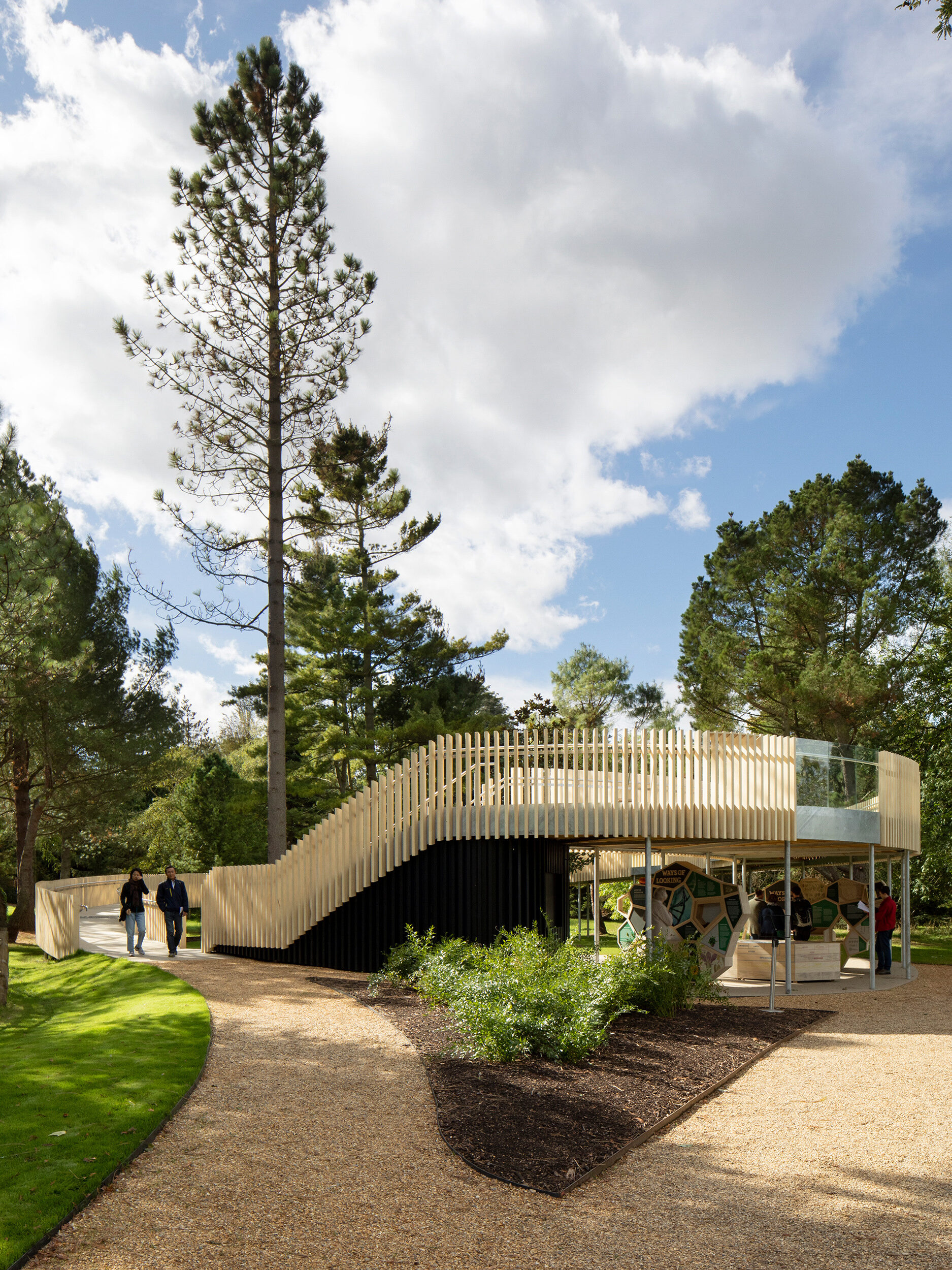 Two people coming off of the Rising Path by architects CDC studios, as viewed from the front. Two others observe the interpretation hub. |  Cambridge University Botanic Garden